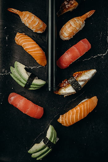 Elegant flat lay of assorted sushi pieces on a dark marble surface with chopsticks. HD phone wallpaper