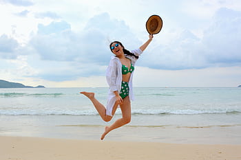 Woman jumps joyfully on a Phuket beach in summer, embodying care vacation spirit. HD wallpaper