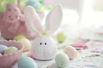 Charming Easter setup featuring a bunny decoration and pastel eggs on a floral tablecloth. HD wallpaper