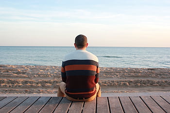 A man sitting on a wooden pier overlooking the tranquil ocean horizon. HD wallpaper