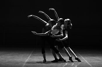 Three female ballerinas perform a synchronized dance on stage in dramatic lighting. HD wallpaper