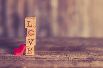 Wooden blocks spelling 'LOVE' with a red heart on a rustic table. HD wallpaper