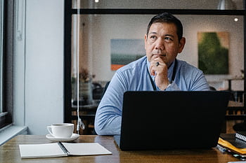 A businessman deep in thought while working on a laptop in a modern office setting. HD wallpaper