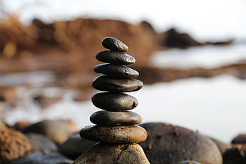 A stack of smooth stones artfully balanced by a waterside, evoking tranquility and zen. HD wallpaper