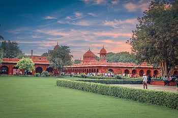 A scenic view of the Red Fort gardens in Delhi, showcasing its historic architecture and lush greenery at sunset. HD wallpaper