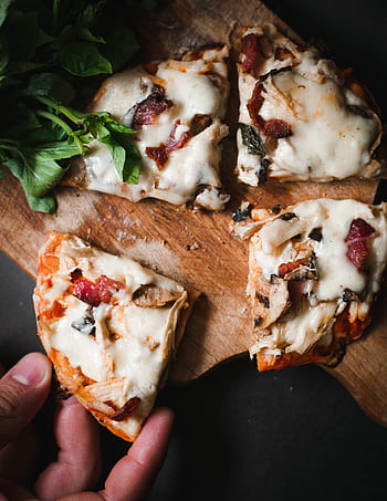 Delicious pizza slices with mozzarella, bacon, and herbs on a wooden board. HD phone wallpaper