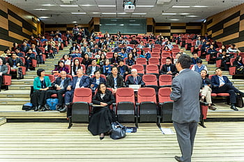 Professional setting of a business conference with attendees and a presenter in an auditorium. HD wallpaper