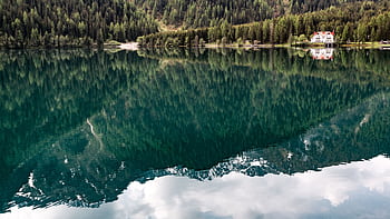 A serene mountain lake scene with a house, surrounded by lush trees reflecting in calm waters. HD wallpaper