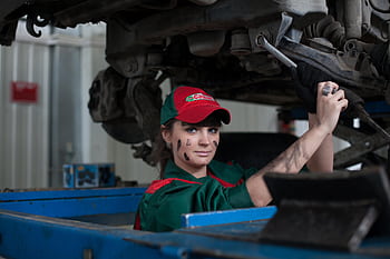 Female mechanic maintaining a car in an auto repair shop, showcasing skill and concentration. HD wallpaper