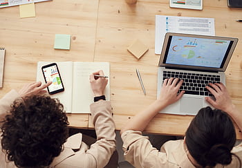 Overhead shot of two colleagues collaborating with devices and notes in a business meeting. HD wallpaper