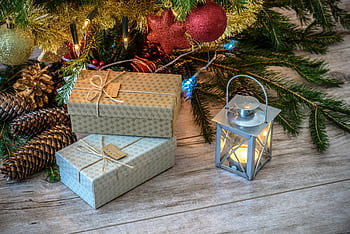 Cozy Christmas scene with wrapped gifts, glowing lantern, and decorated tree branches on wood floor. HD wallpaper
