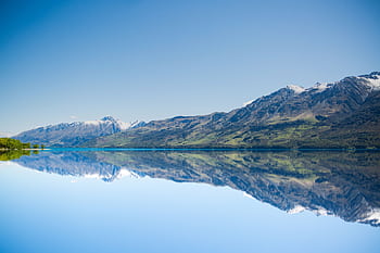 Stunning reflection of mountains on a calm lake under a clear blue sky, showcasing natural beauty. HD wallpaper