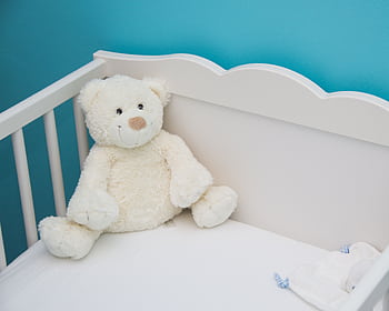 Soft teddy bear in a white crib against a vibrant blue wall, creating a comforting nursery atmosphere. HD wallpaper