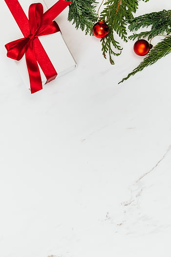 Top-down view of a white gift with red ribbon and evergreen branches, perfect for holiday themes. HD phone wallpaper