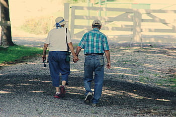 Senior couple holding hands and walking outdoors on a gravel path, showcasing love and companionship. HD wallpaper
