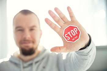 A man in a hoodie holds up his hand with a 'Stop and Pray' sticker. Focus on hand and sticker. HD wallpaper