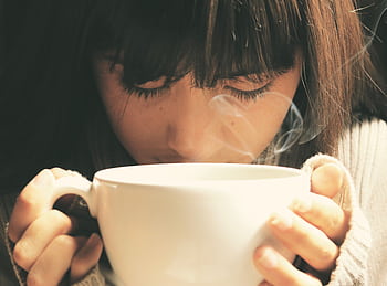 Woman savoring the aroma of a hot coffee cup in a cozy setting. HD wallpaper