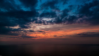 A vibrant sunset with dramatic clouds over a calm ocean. Perfect for serene and atmospheric visuals. HD wallpaper