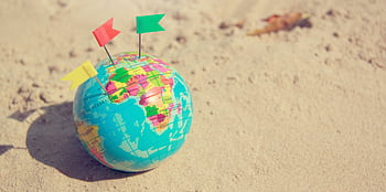 A vibrant globe with pins on a sandy surface, symbolizing travel plans. HD wallpaper