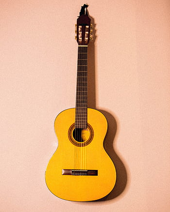 Yellow acoustic guitar hanging on a wall, showcasing its design and craftsmanship. HD phone wallpaper