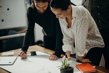 Two colleagues engage in a creative brainstorming session at the office, working together on new ideas. HD wallpaper