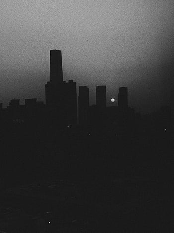 Atmospheric black and white urban skyline with silhouetted buildings and a setting sun. HD phone wallpaper