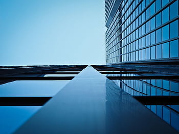 Low angle view of a modern skyscraper with reflective glass facade and blue sky. HD wallpaper