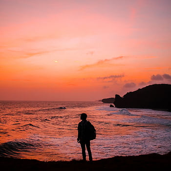 Silhouette of a person with a backpack against a vibrant Indonesian sunset by the sea. HD phone wallpaper
