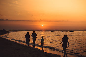 A family walking along Mandra beach, Greece, silhouetted against a stunning sunset. HD wallpaper