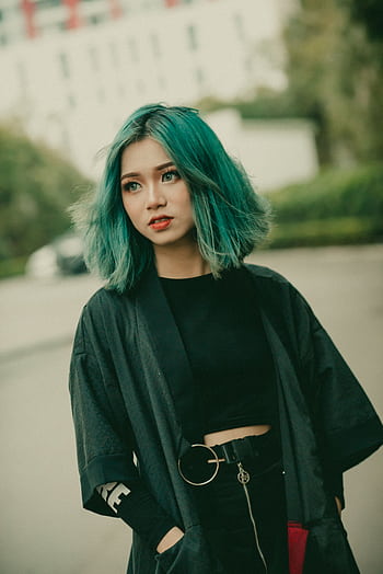 A fashionable young woman with teal hair poses outdoors in an urban area, displaying a modern and stylish look. HD phone wallpaper