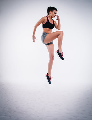 Woman in black sports bra and gray shorts performing a jump during workout. HD phone wallpaper