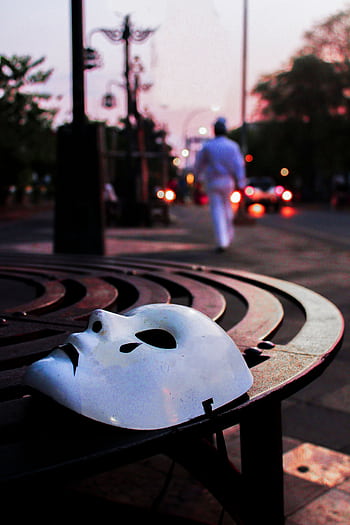 A solitary white mask on a circular bench at dawn in a quiet urban street. HD phone wallpaper