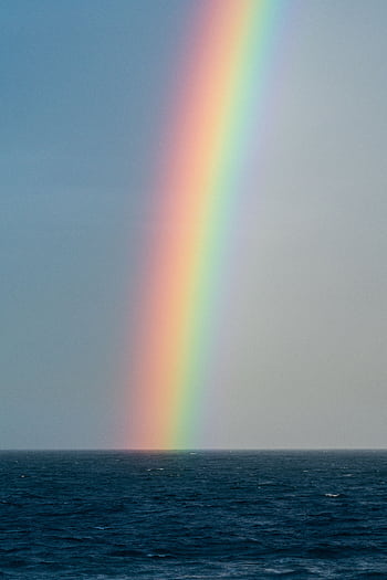 A stunning rainbow arches over the ocean, creating a vivid and peaceful seascape. HD phone wallpaper
