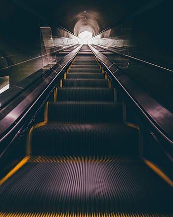 A captivating view of a modern escalator leading upwards in a dimly lit indoor tunnel. HD phone wallpaper