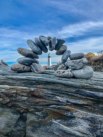 A serene of balanced stones with the iconic Portland Head Lighthouse in the background. HD phone wallpaper