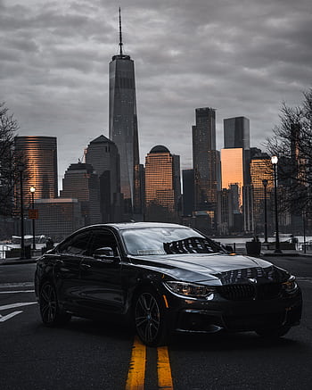 Sleek luxury car on a city road with the iconic New York skyline glowing at sunset. HD phone wallpaper