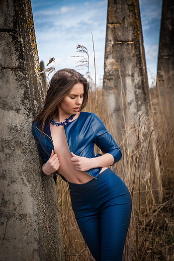 Fashion model in blue leather jacket posing against stone pillars outdoors. HD phone wallpaper