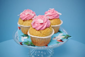 Three homemade cupcakes with pink frosting on a glass stand, perfect for dessert and parties. HD wallpaper
