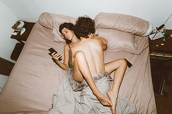 A couple in bed looking at smarts, highlighting modern disconnection. HD wallpaper