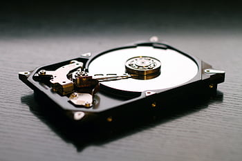 An open hard drive is displayed on a wooden surface, showcasing its internal components and metallic details. HD wallpaper