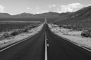 Black and white view of a long, empty highway stretching into distant desert mountains. HD wallpaper