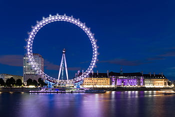 The illuminated London Eye reflects over the River Thames at night, showcasing vibrant city lights. HD wallpaper