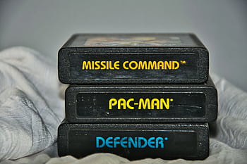 Close-up of vintage Atari game cartridges for Missile Command, Pac-Man, and Defender. HD wallpaper