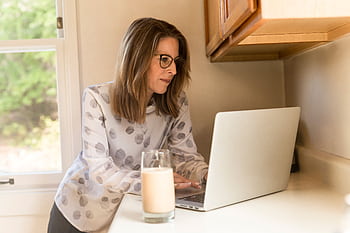 A woman working on a laptop in a home kitchen, illustrating remote work lifestyle. HD wallpaper