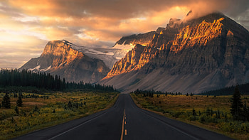 Road Between Bushes Trees Grass Field And Landscape View Of Rock Mountains With Snow During Sunset Nature HD wallpaper