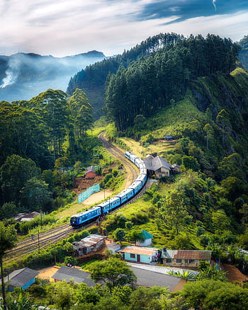 Aerial view of a que train winding through lush green hills and rural houses. HD phone wallpaper