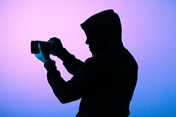 A silhouette of a hooded grapher capturing a shot with a camera in a softly lit studio. HD wallpaper