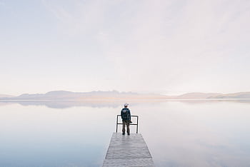 A solitary traveler stands on a dock enjoying the serene water view HD wallpaper