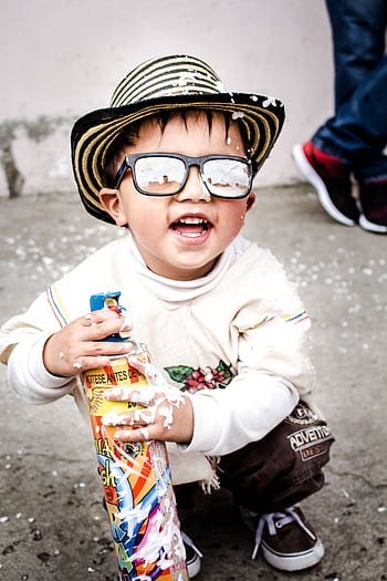 Happy child wearing sunglasses and a hat playing with foam spray in Colombia. HD phone wallpaper
