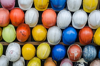 Vibrant collection of industrial safety helmets neatly arranged on a wall. HD wallpaper